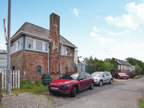 A red car parked in front of a brick building with a chimney.