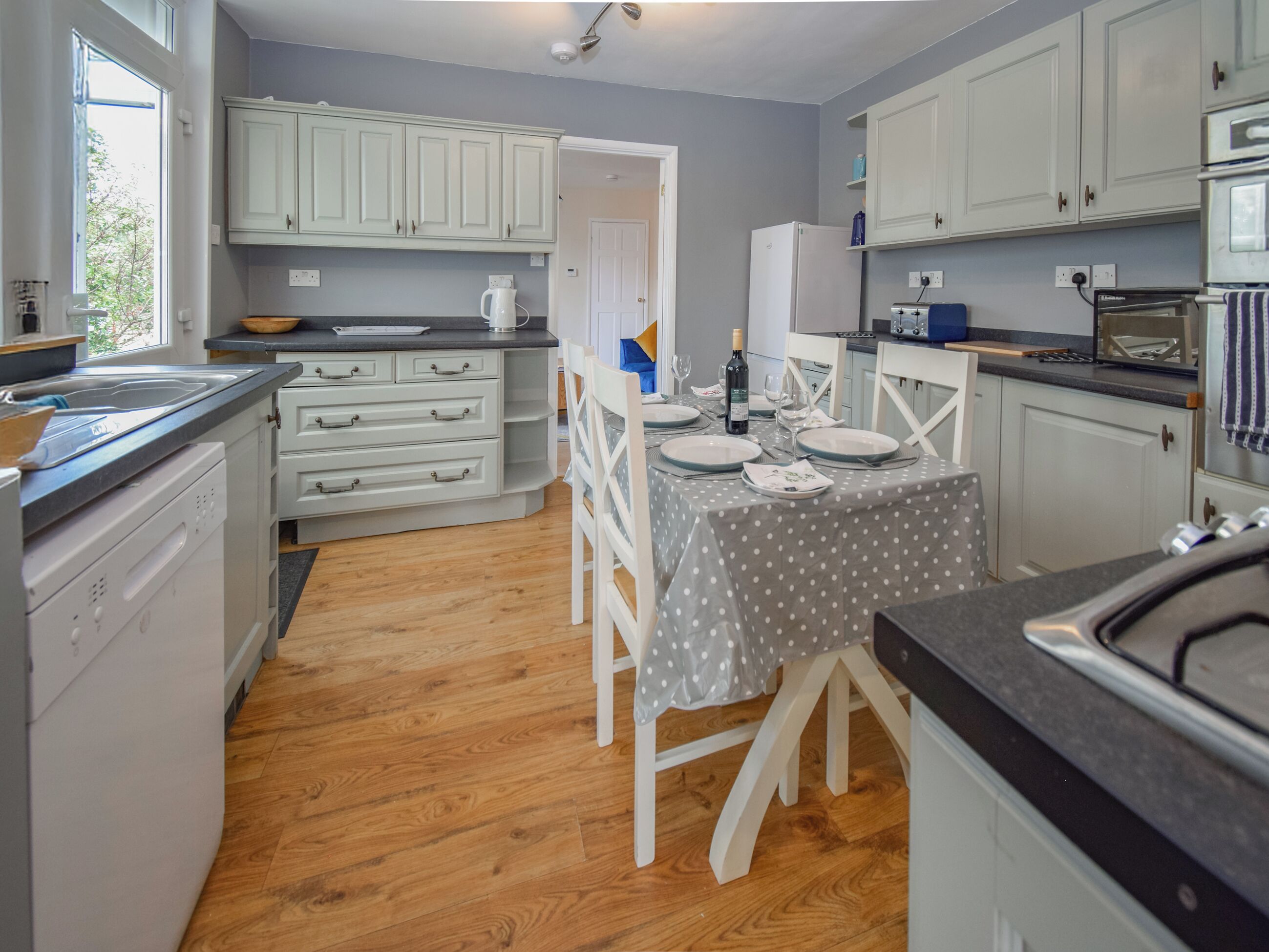 A compact kitchen with white cabinets, a dining table set for two, and a wooden floor.