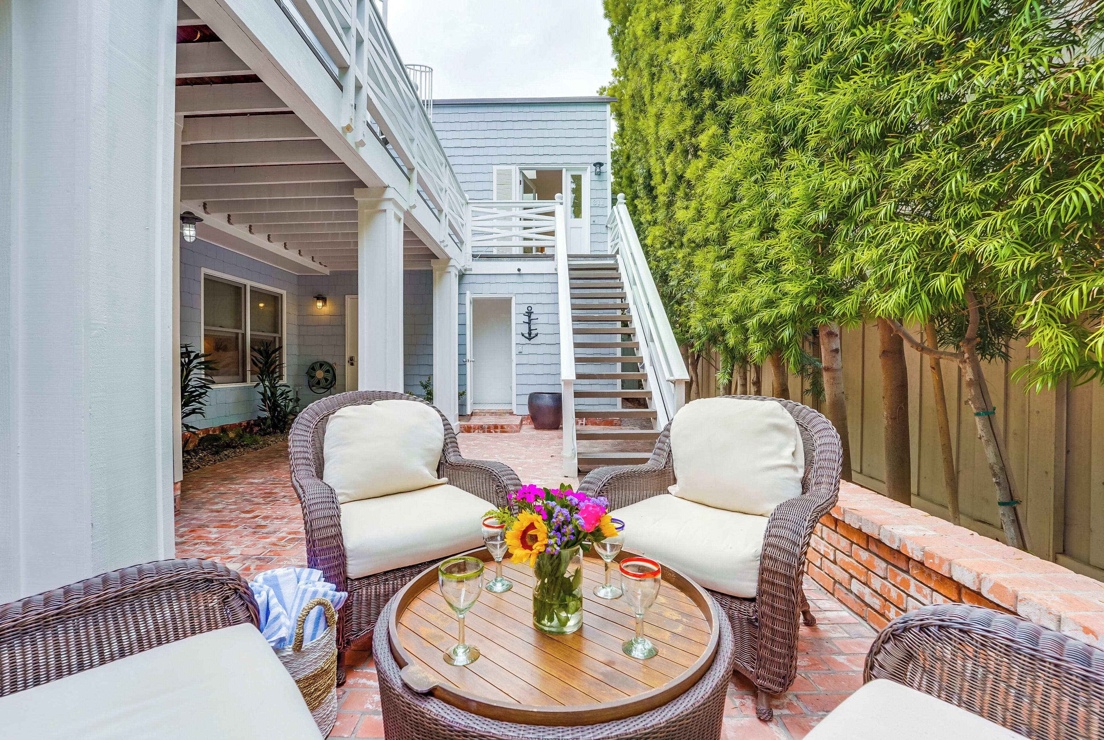 A patio with wicker furniture, a round wooden table, and a staircase leading to an upper level.