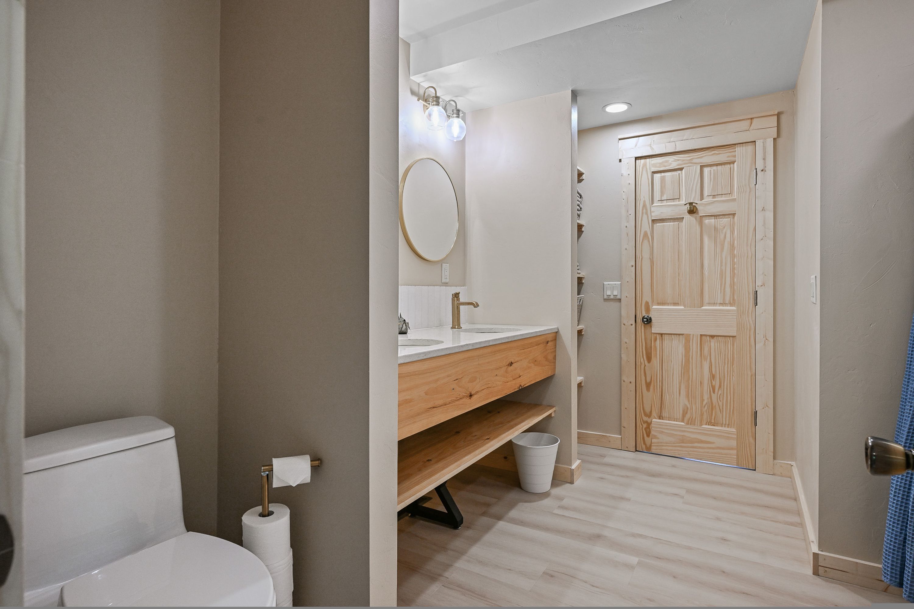 A bathroom with a toilet, sink, mirror, and wooden door.