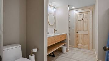 A bathroom with a toilet, sink, mirror, and wooden door.