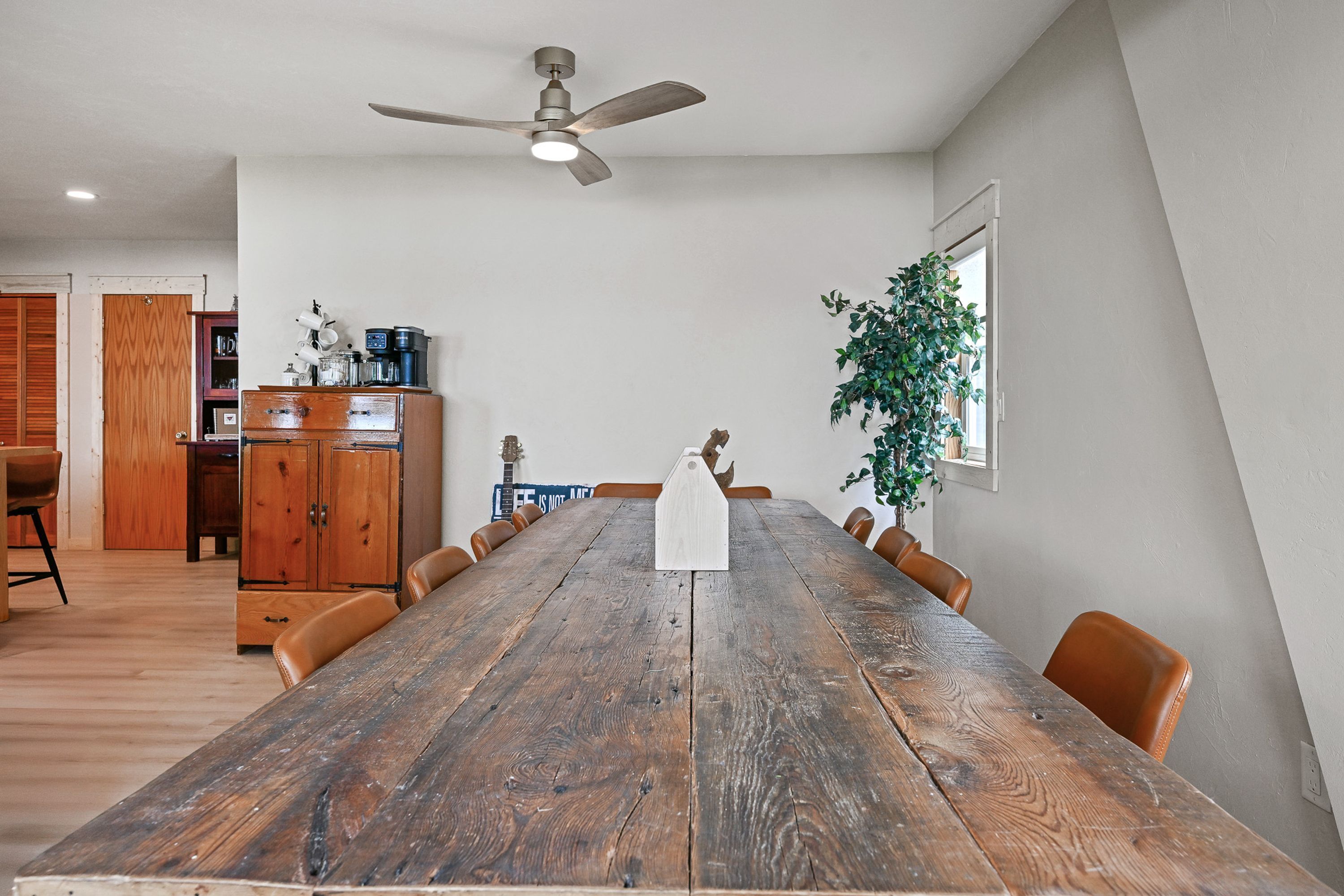 A dining area with a wooden table, chairs, a ceiling fan, and a potted plant.