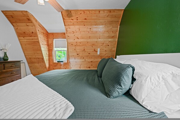 A bedroom with a sloped ceiling, wooden walls, a bed with green bedding, and a dresser.