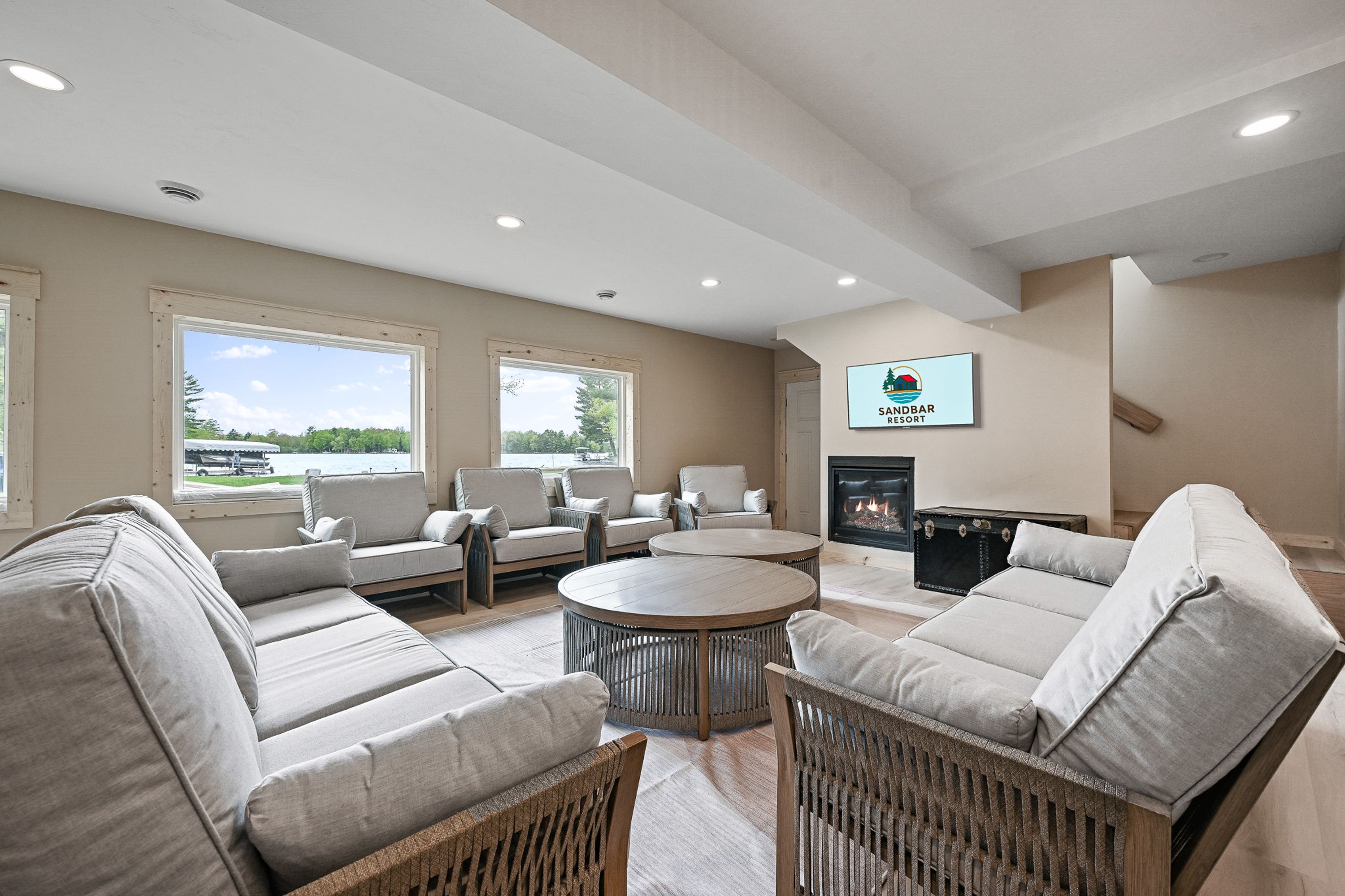 A spacious living room with a fireplace, large windows, and a sign for Sandbar Resort.