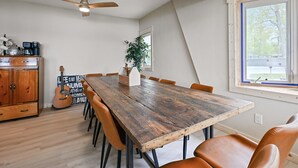 Un comedor con una mesa y sillas de madera, un ventilador de techo y vistas al exterior a través de una ventana.