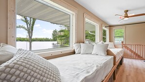 Un dormitorio con dos camas, ventanas amplias, ventilador de techo y vista al lago.