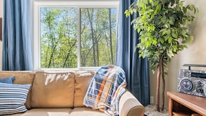 A living room with a beige sofa, a plaid blanket, a radio, and a potted plant. - Sauna| Garage Golf Games| Close to shopping (Pequot Lakes)