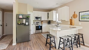 A modern kitchen with white cabinets, stainless steel appliances, and a central island with bar stools. - Sauna| Garage Golf Games| Close to shopping (Pequot Lakes)