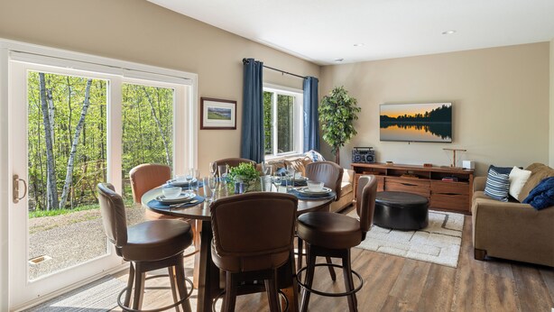 A spacious living room with a dining area, large windows, and a view of the outdoors. - Sauna| Garage Golf Games| Close to shopping (Pequot Lakes)