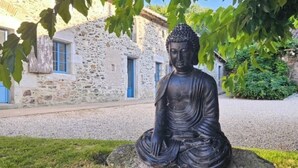 A seated Buddha statue in a garden with stone buildings in the background. - Exceptional eco-domain (spa&pool) (Le retail)