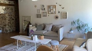 A cozy living room with a sofa, a coffee table, and a chair. There are wall decorations and a plant on a side table. - Exceptional eco-domain (spa&pool) (Le retail)