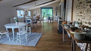 A spacious dining area with a wooden floor, white round table, and chairs. A buffet table with various dishes is visible on the right. - Exceptional eco-domain (spa&pool) (Le retail)