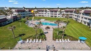 A hotel with a swimming pool, lounge chairs, and palm trees.