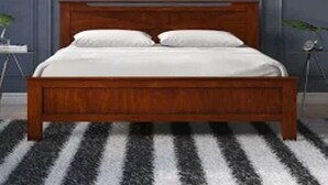 Un lit avec une tête de lit en bois, une literie blanche et un tapis rayé noir et blanc.