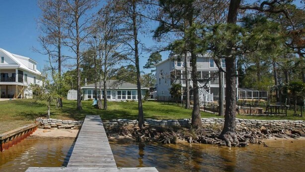 En träbrygga som leder fram till en flodbank, med hus i bakgrunden.