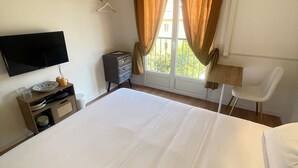 A hotel room with a bed, a TV, a desk, a chair, a wardrobe, and a window with curtains. - Apparthôtel New Palmarium (Amélie-les-Bains-Palalda)
