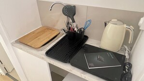 A compact kitchen with a wooden cutting board, a black electric kettle, a coffee maker, and a small white refrigerator. - Apparthôtel New Palmarium (Amélie-les-Bains-Palalda)