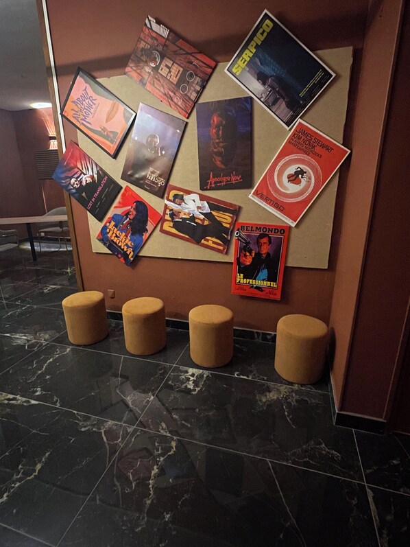 Eine Schwarztafel mit verschiedenen Filmplakaten, einem Marmorboden und vier Hockstühlen.