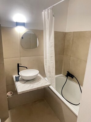 Ein Badezimmer mit einem weißen Waschbecken, einem runden Spiegel, einer Duschvorhang und einer Badewanne.