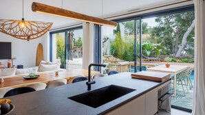 Une cuisine moderne dotée d’un grand îlot central, d’un coin repas avec une table et des chaises, et offrant une vue sur une piscine extérieure.