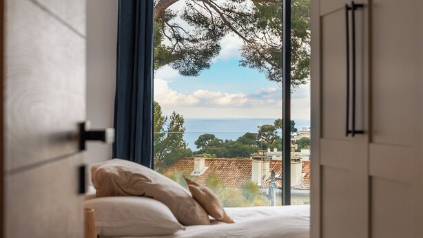 Une chambre à coucher avec un lit, des oreillers et une vue sur la mer et les bâtiments.