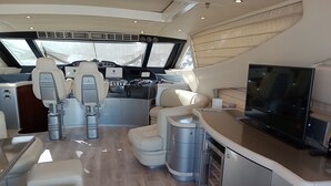 Het interieur van een jacht met een bedieningspaneel, zitplaatsen, een televisie en een kombuis.