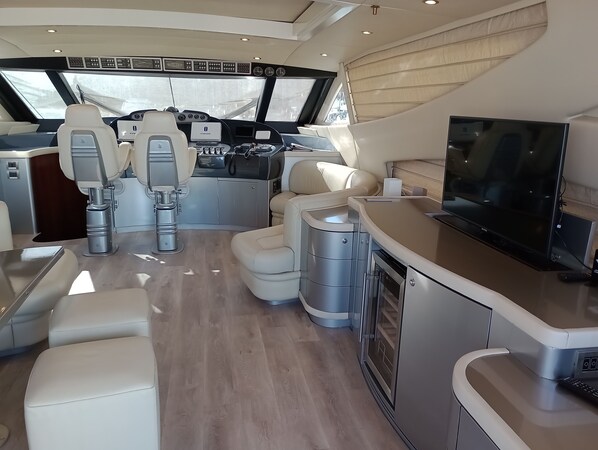 A yacht's interior with a control panel, seating, a TV, and a galley area.