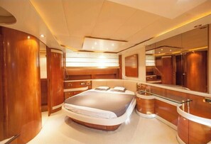 A luxurious bedroom with a large bed, wooden paneling, a glass-enclosed vanity, and a large mirror.