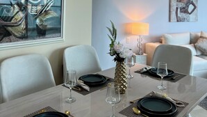 Comedor con una mesa dispuesta para dos personas, con platos negros, cubiertos dorados y un florero con flores.