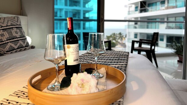 Una cama con una botella de vino, dos copas y una bandeja con una flor.