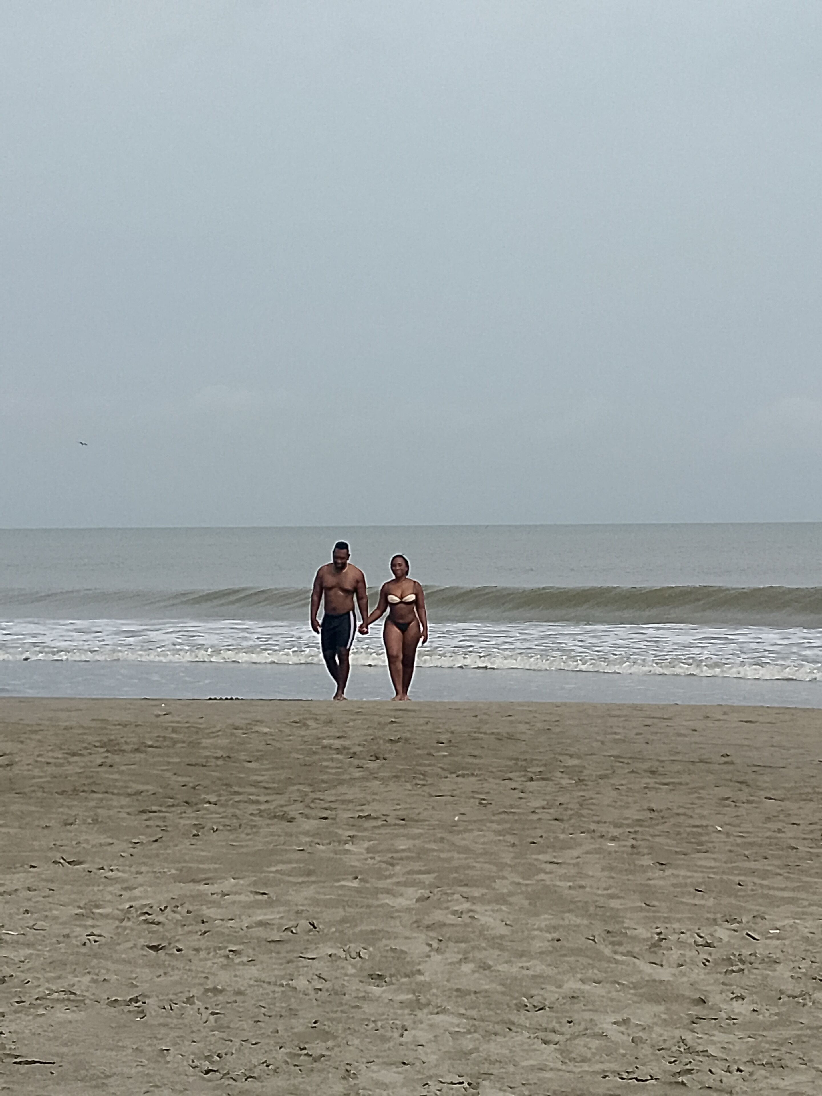 Ein Strand mit zwei Personen, die am Sand entlanggehen.