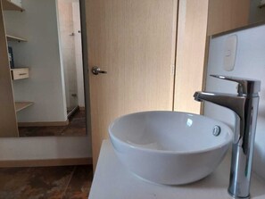 Un baño con un lavamanos de cerámica blanca, una puerta de madera y un espejo.