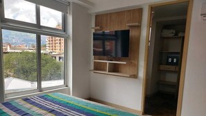 Un dormitorio con cama, televisor montado en la pared y vistas a edificios.