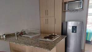 Una cocina con encimera de granito, refrigerador de acero inoxidable y armarios de madera.
