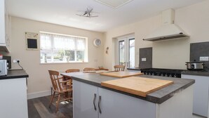 A modern kitchen with a central island, wooden chairs, a stove, and a window with curtains. - Fishermans Cottage (Withernsea)