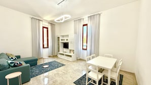 Un salon moderne comprenant un canapé, une table à manger avec des chaises, un meuble pour la télévision et une grande fenêtre avec des rideaux.