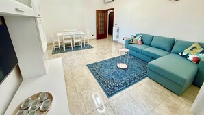 Un salon avec un canapé, une table à manger et des chaises, un téléviseur et une horloge au mur.