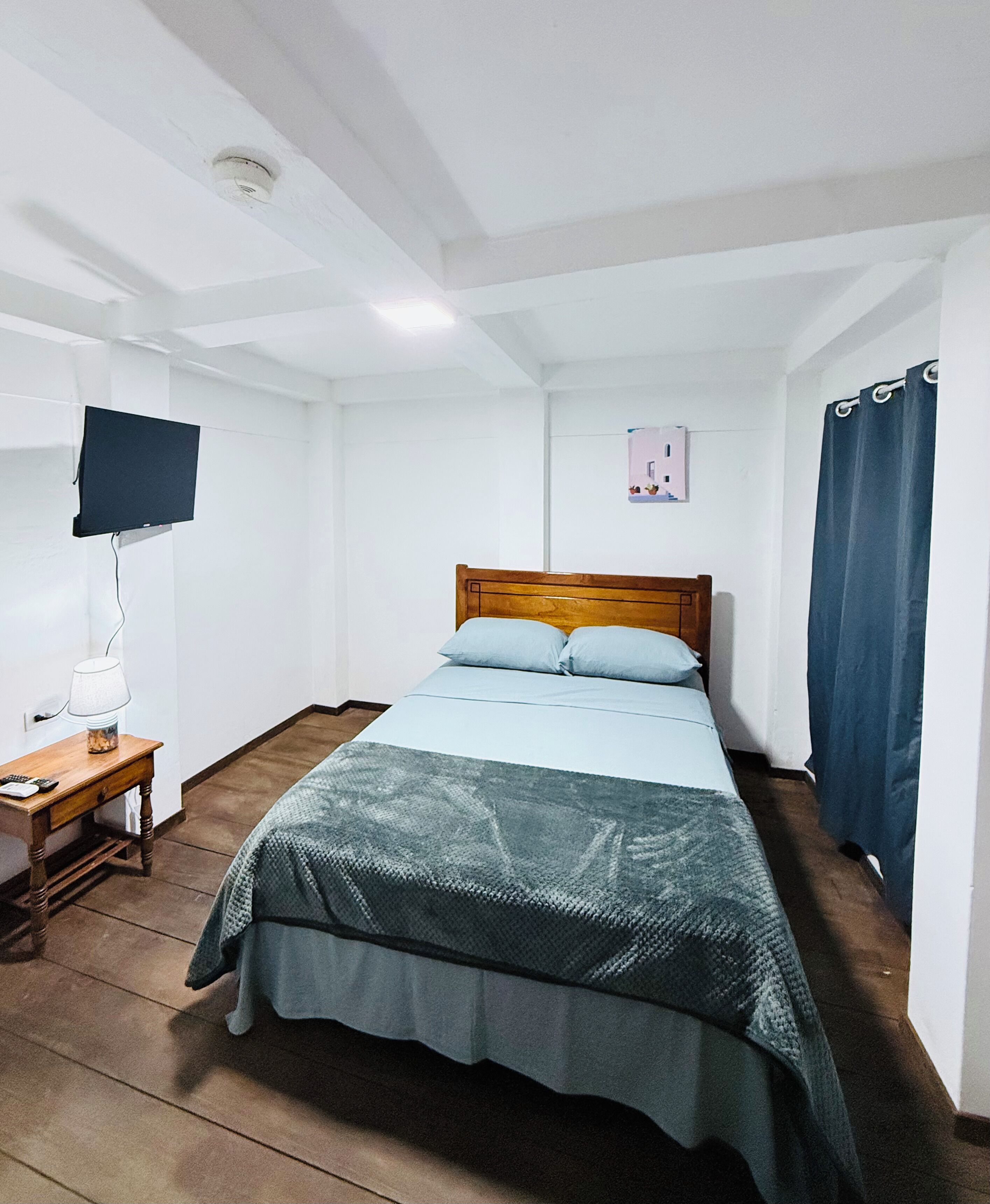 Una habitación pequeña y sencilla con una cama, un escritorio y un televisor.