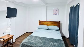 Una habitación pequeña y sencilla con una cama, un escritorio y un televisor.