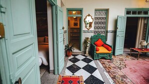 Una stanza con pavimento a scacchi, una poltrona verde con cuscini arancioni, una parete decorata e una porta che dà su un'altra stanza.