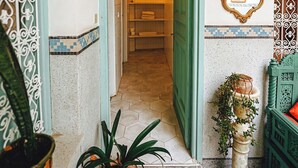 Un corridoio con una porta verde che dà su una stanza con pavimento piastrellato e lampadario.