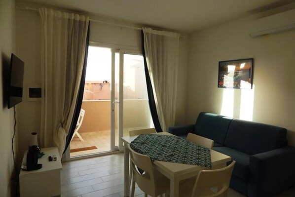 A room with a sofa, a table, a TV, and a balcony.