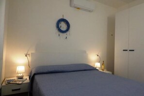 A neatly made bed with a blue blanket, a bedside lamp, a wall-mounted air conditioner, and a closed wardrobe.