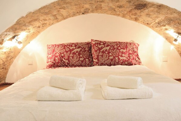 A bed with white linens, two red patterned pillows, and two rolled white towels. - Stay in a real medieval tower (lower floors) (Tallinn)