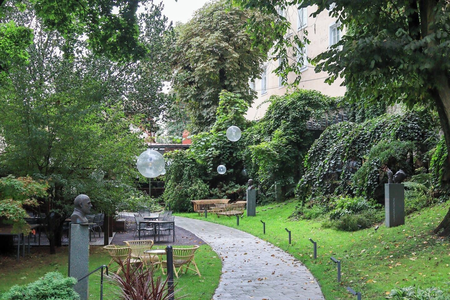 Un jardin avec un chemin pavé, des sièges extérieurs et des sculptures.