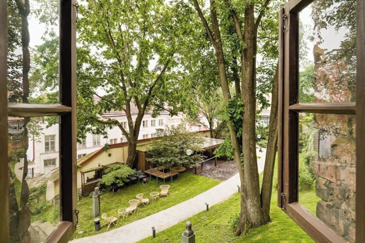 Une vue à travers une fenêtre donnant sur une cour avec une pelouse, un espace aménagé pour s’asseoir et des arbres.