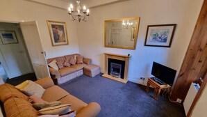 Una sala de estar con sofá, chimenea, televisor y candelabro.