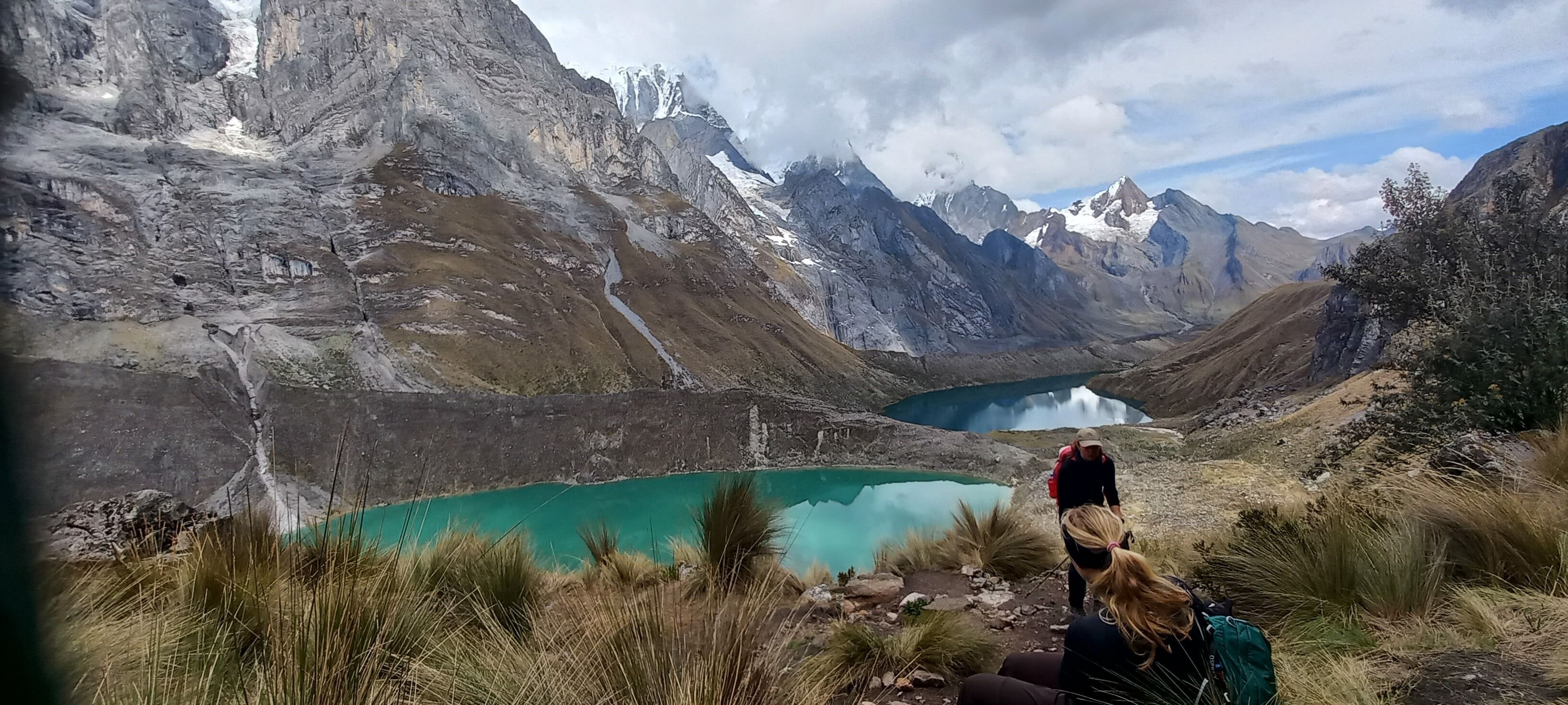 Un paisaje montañoso con un lago turquesa y una persona haciendo senderismo.