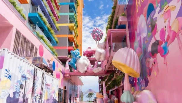 A narrow street with colorful buildings, a pink wall with a mural, and a variety of decorative items like balloons and plush toys. - Flamingo Bau Abtel (Hoang Tien)