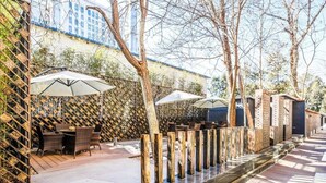 An outdoor patio area with wooden flooring, a seating arrangement with chairs and tables, and umbrellas providing shade. - Qiuguo Hotel Beijing by Bayluxury (Beijing)